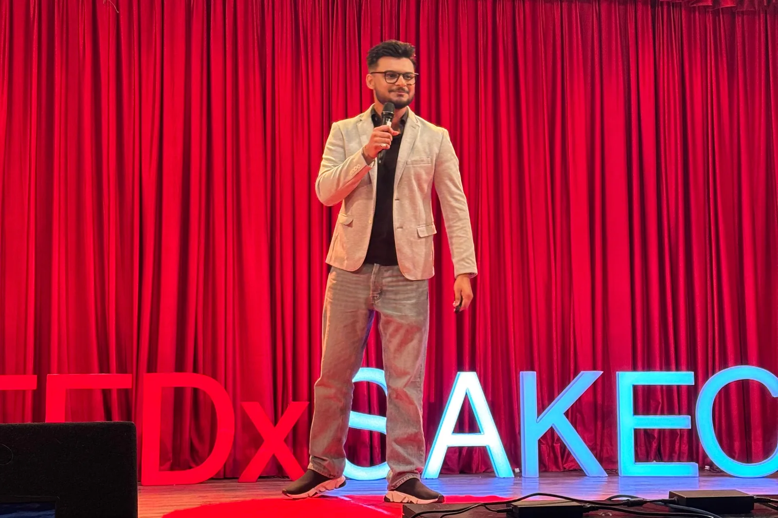 Sidhant Kisshor speaking at TEDxSAKEC, with the event sign behind him